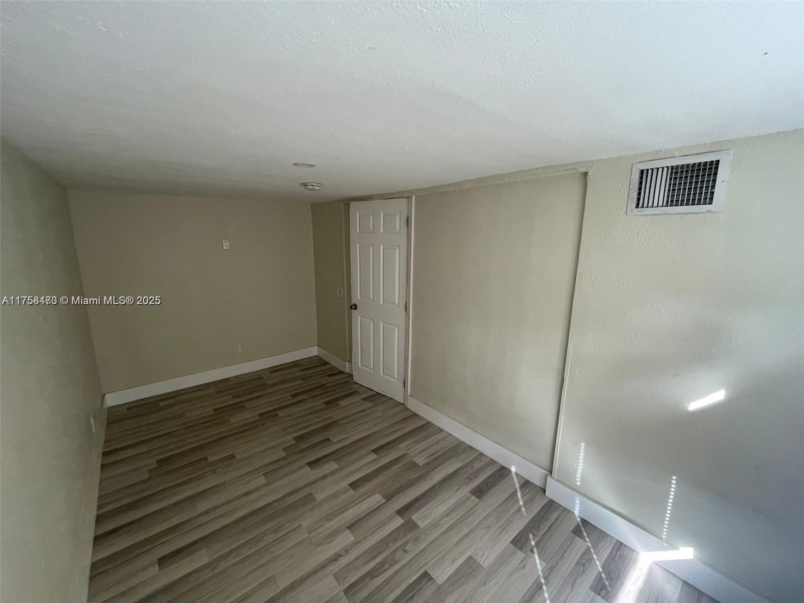 An empty room features light-colored walls, wood-look flooring, and a single white interior door — 4896 SW 28th Ter, Dania Beach FL 33312, DANIA BEACH, FL