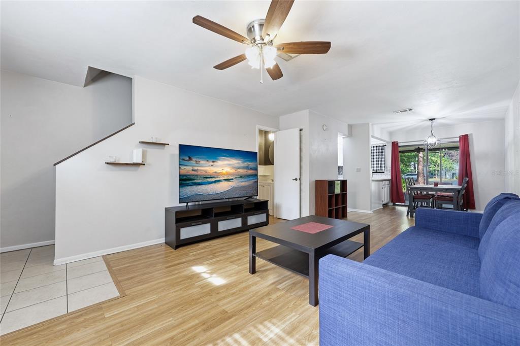 A living room features light wood flooring, a blue sofa, a television, and a ceiling fan — 4128 NW 44TH DRIVE, GAINESVILLE, FL