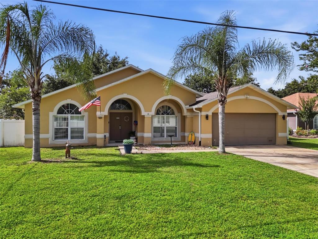 A single-story tan house with a two-car garage, arched windows, and two palm trees — 10 LARKSPUR WAY, PALM COAST, FL
