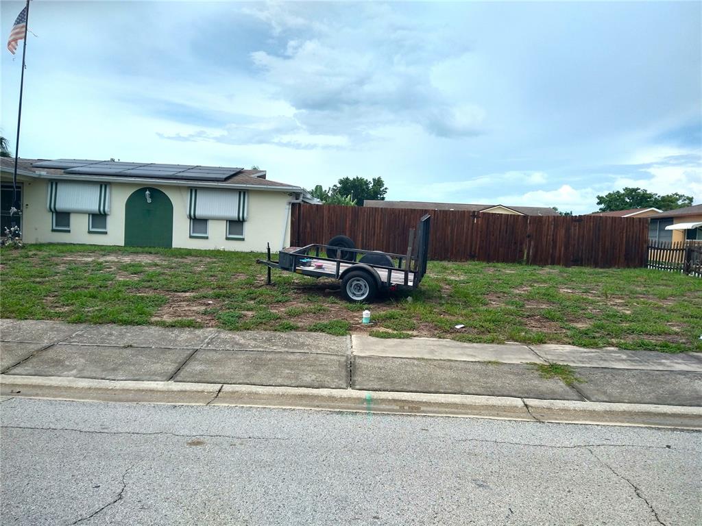 A utility trailer sits on a grassy lot next to a house with solar panels — 6325 KENTFIELD AVENUE, NEW PORT RICHEY, FL