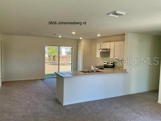 An open-concept kitchen with white cabinets and a breakfast bar overlooks a carpeted living area — 3856 JOHANNESBERG ROAD, NORTH PORT, FL