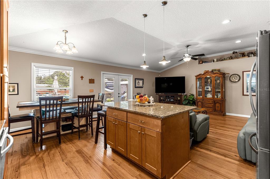 A kitchen with a granite-topped island, wooden cabinets, and an adjacent dining area — 4328 CHOKEBERRY, MIDDLEBURG, FL