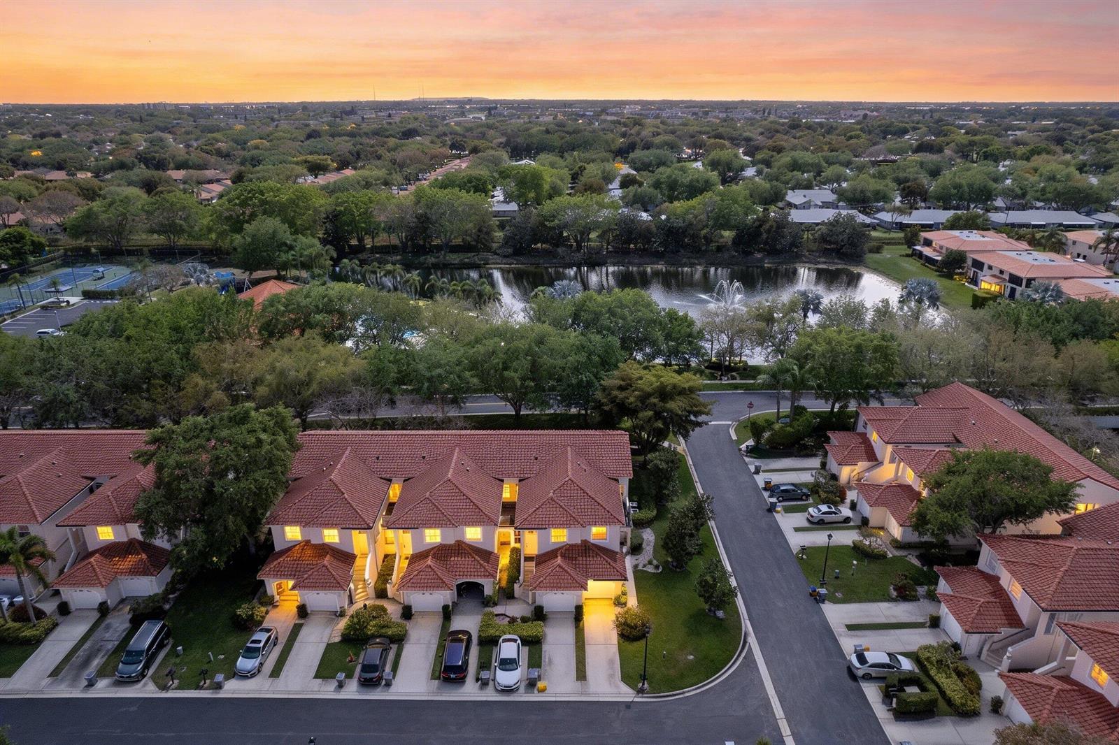 An aerial view of a residential complex with townhomes, a lake, and a fountain at sunset — 8550 Via Romana # 1, Boca Raton FL 33496, BOCA RATON, FL