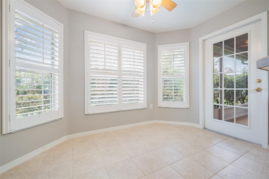 A sunroom with light-colored tile flooring, plantation shutters on the windows, and a glass-paneled door — 10230 OLD TAMPA BAY DRIVE, SAN ANTONIO, FL