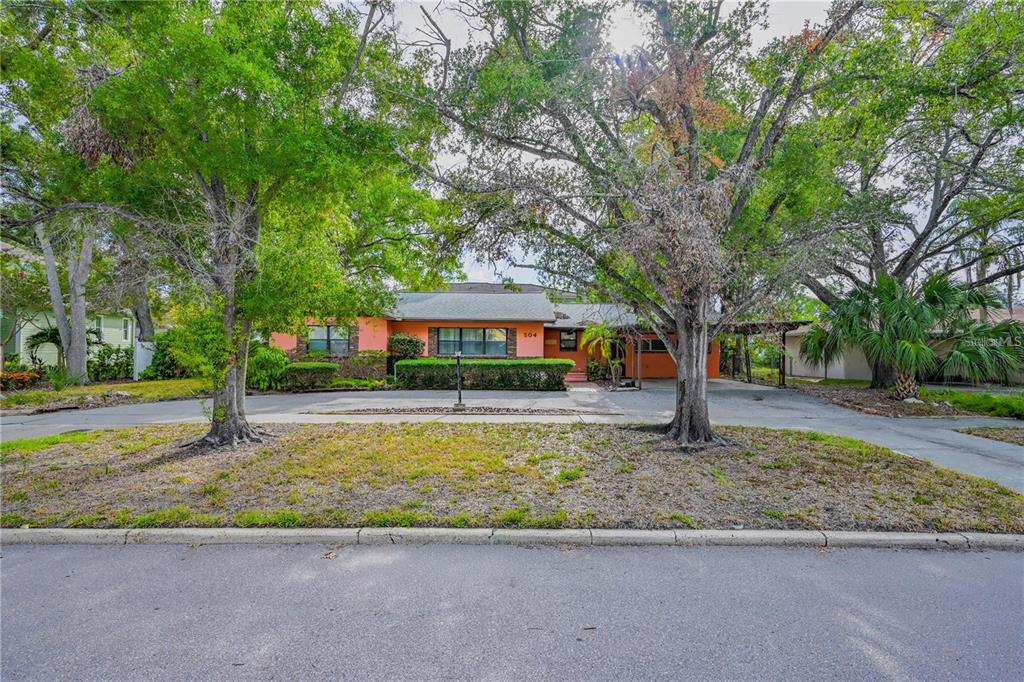 A single-story orange house with a large driveway and mature trees in the front yard — 504 W DAVIS BOULEVARD, TAMPA, FL