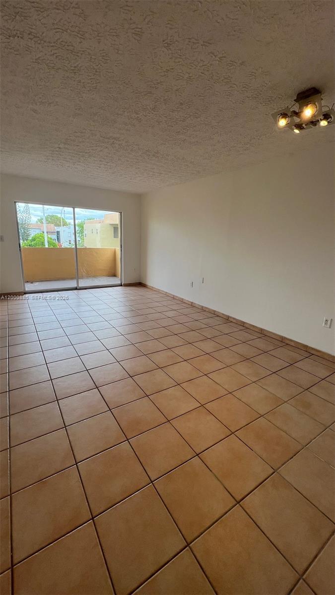 An empty room features beige tile flooring, white walls, and a sliding glass door to a balcony — 6070 W 18th Ave # 323, Hialeah FL 33012, HIALEAH, FL