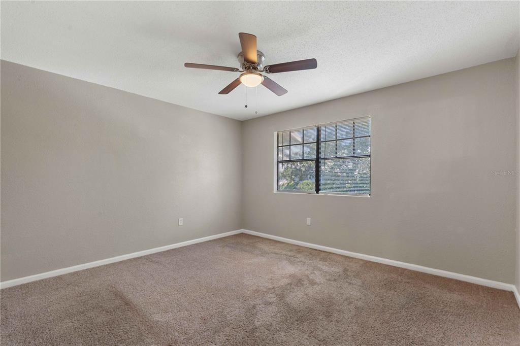 An empty bedroom features beige walls, brown carpeting, a ceiling fan, and a window — 204 PINE TULIP COURT UNIT 201, TAMPA, FL