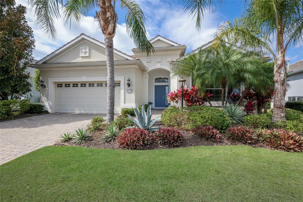A single-story house with a beige stucco exterior, a two-car garage, and landscaped front yard — 14335 STIRLING DRIVE, LAKEWOOD RANCH, FL