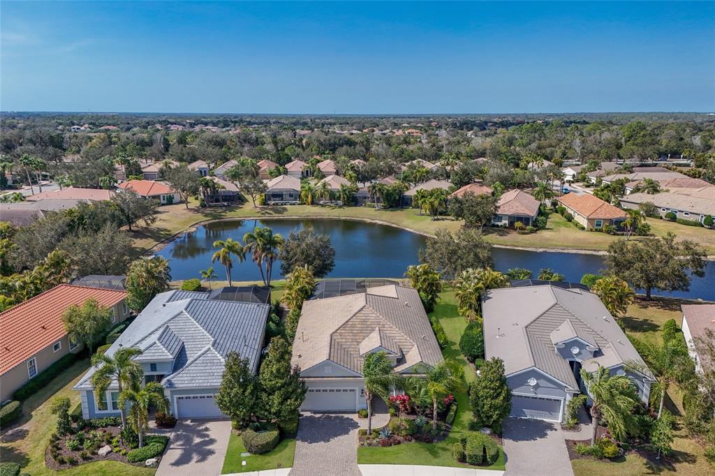An aerial view shows three suburban houses with tiled roofs situated along a small lake — 14335 STIRLING DRIVE, LAKEWOOD RANCH, FL