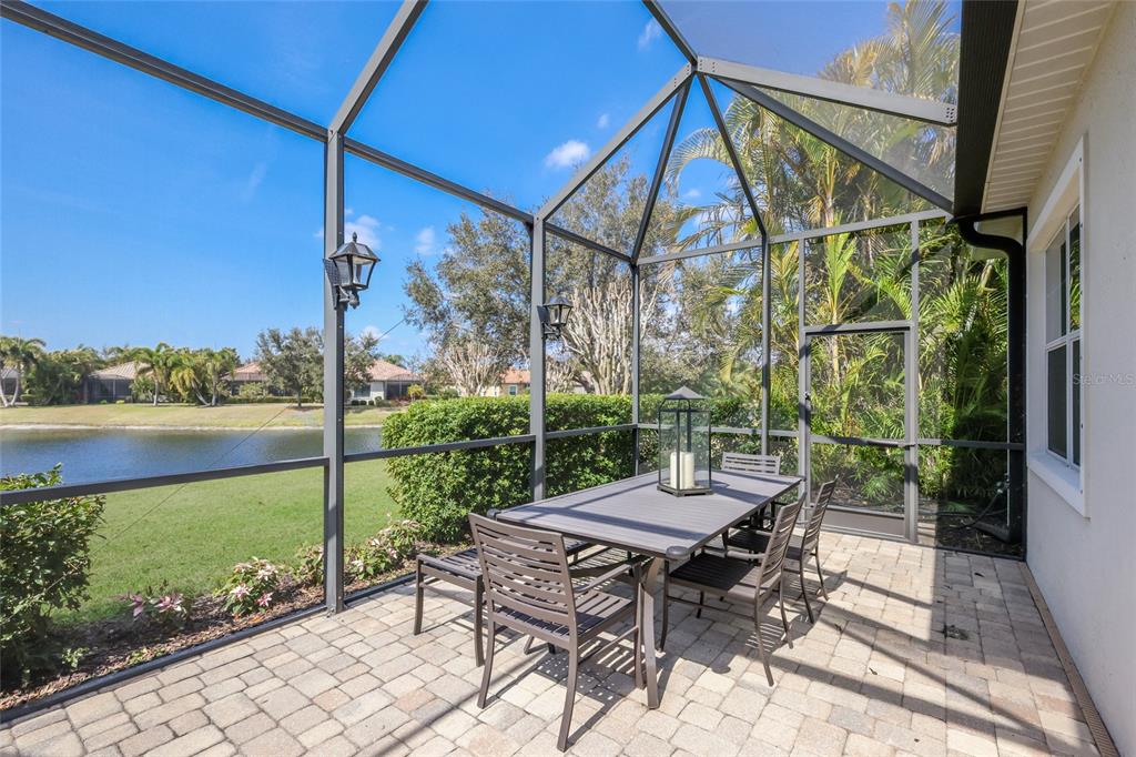 A covered patio features a ceiling fan, outdoor furniture, and a screened-in pool overlooking water — 14335 STIRLING DRIVE, LAKEWOOD RANCH, FL