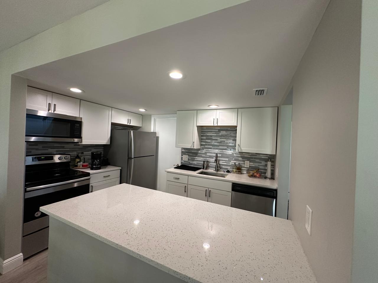 A modern kitchen features white cabinets, stainless steel appliances, a quartz island, and tiled backsplash — 7200 NW 2nd Avenue # 1520, Boca Raton FL 33487, BOCA RATON, FL