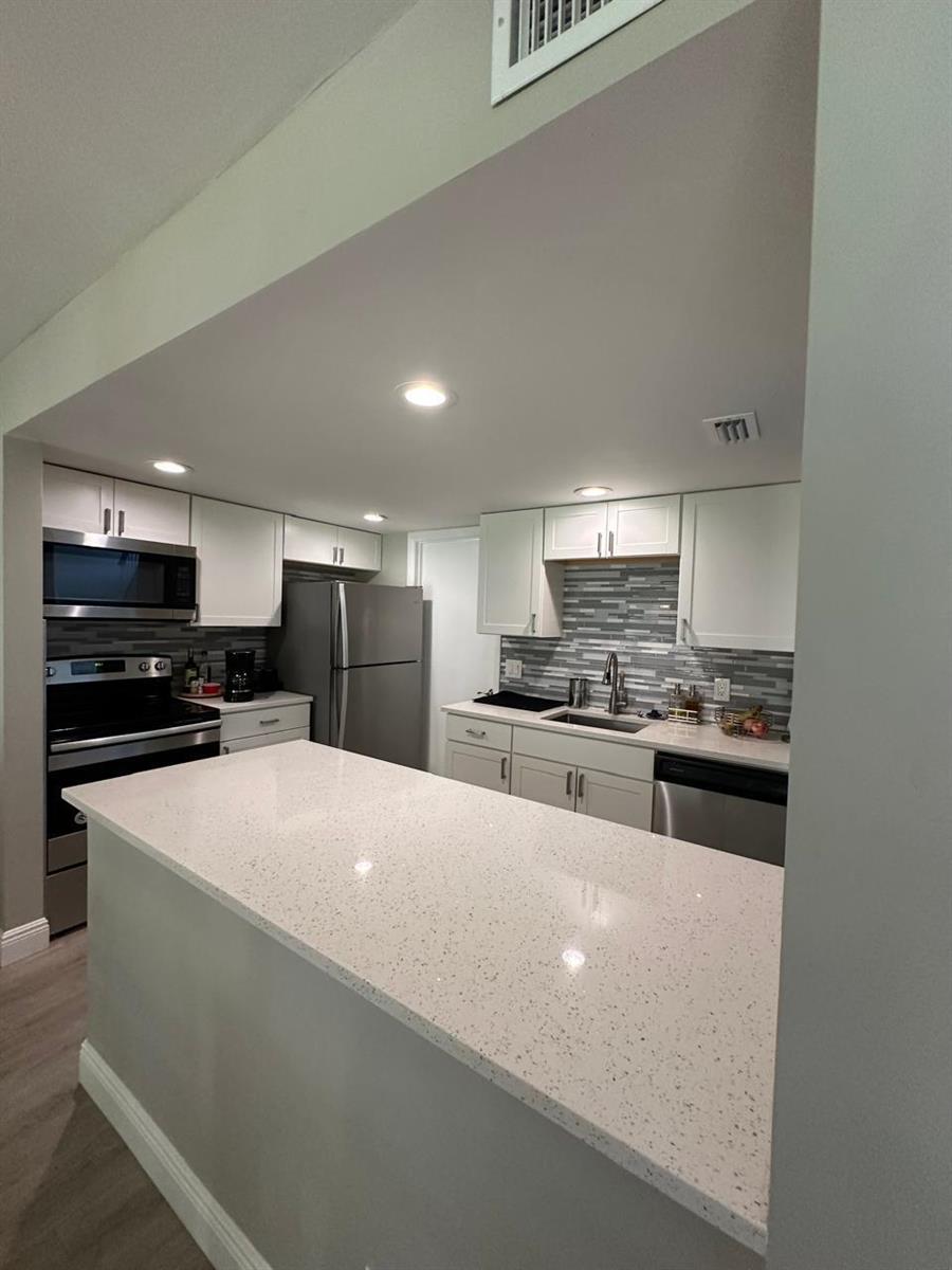A kitchen features white cabinets, quartz countertops, stainless steel appliances, and a gray tile backsplash — 7200 NW 2nd Avenue # 1520, Boca Raton FL 33487, BOCA RATON, FL