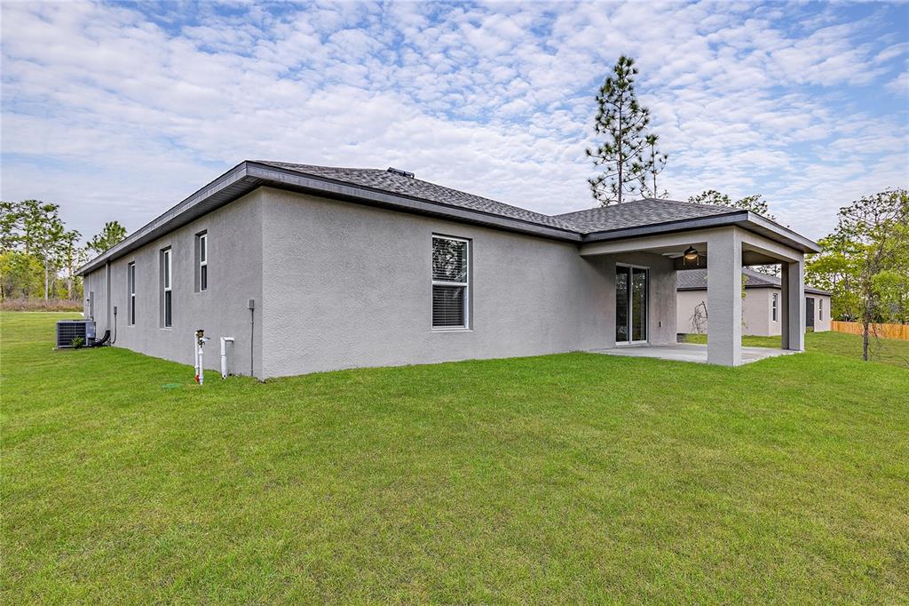 The exterior of a gray stucco house features a covered patio and a grassy yard — 7220 SWARTBURG ROAD, NORTH PORT, FL