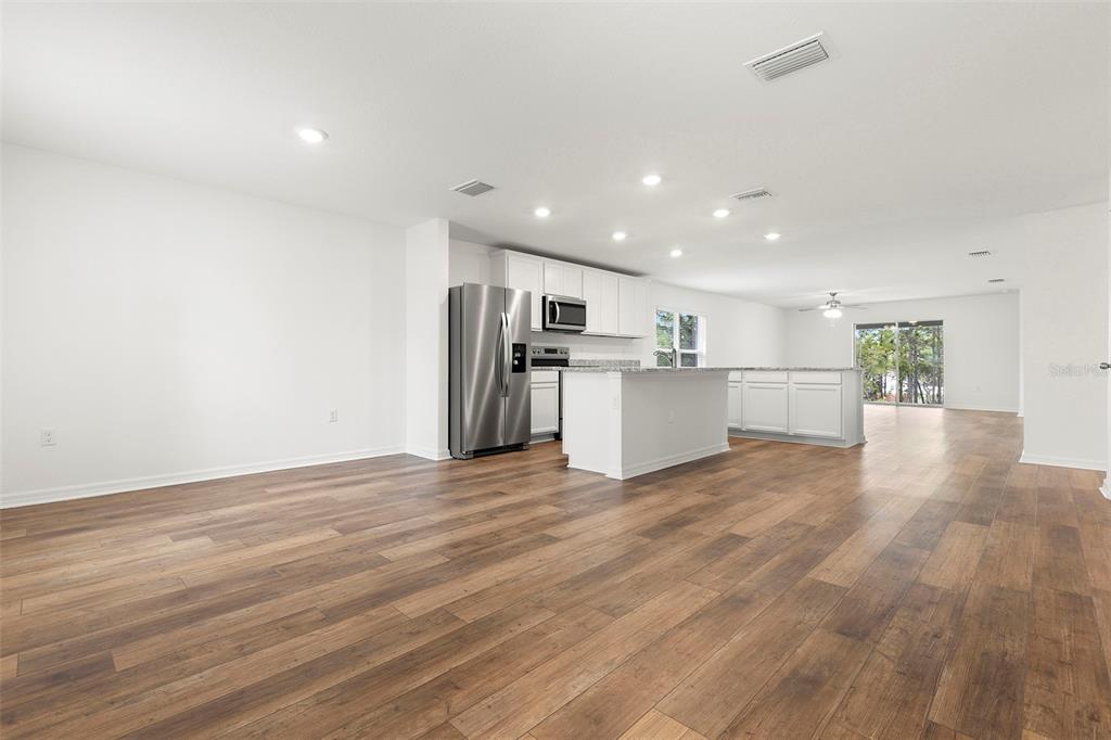 An open-concept kitchen with white cabinets, stainless steel appliances, and wood-look flooring — 7220 SWARTBURG ROAD, NORTH PORT, FL