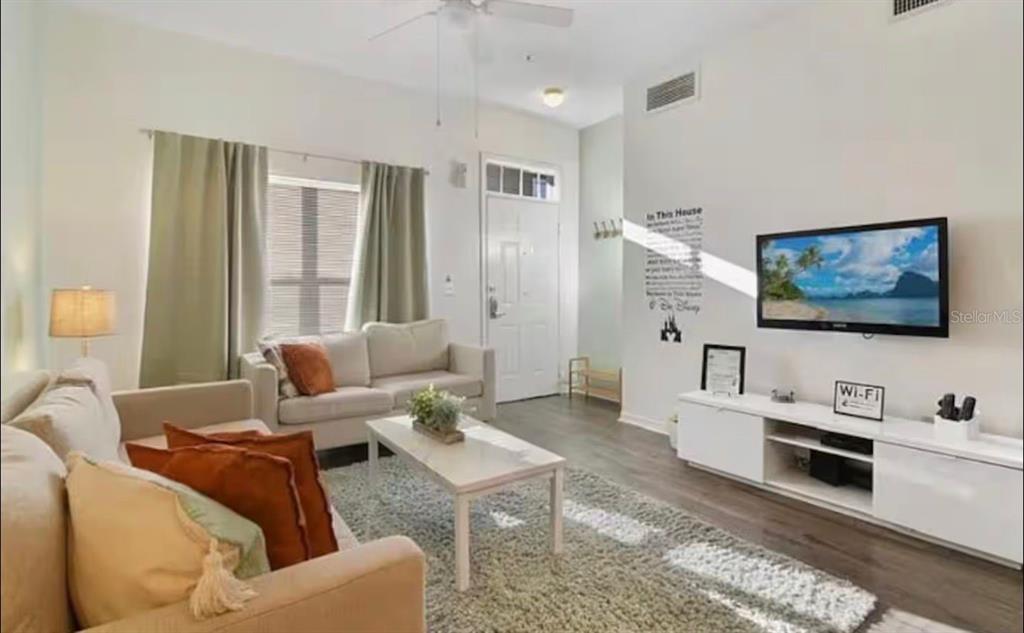 A living room features a sofa, coffee table, area rug, and a wall-mounted television — 4560 E YELLOWGOLD ROAD APT 105, KISSIMMEE, FL