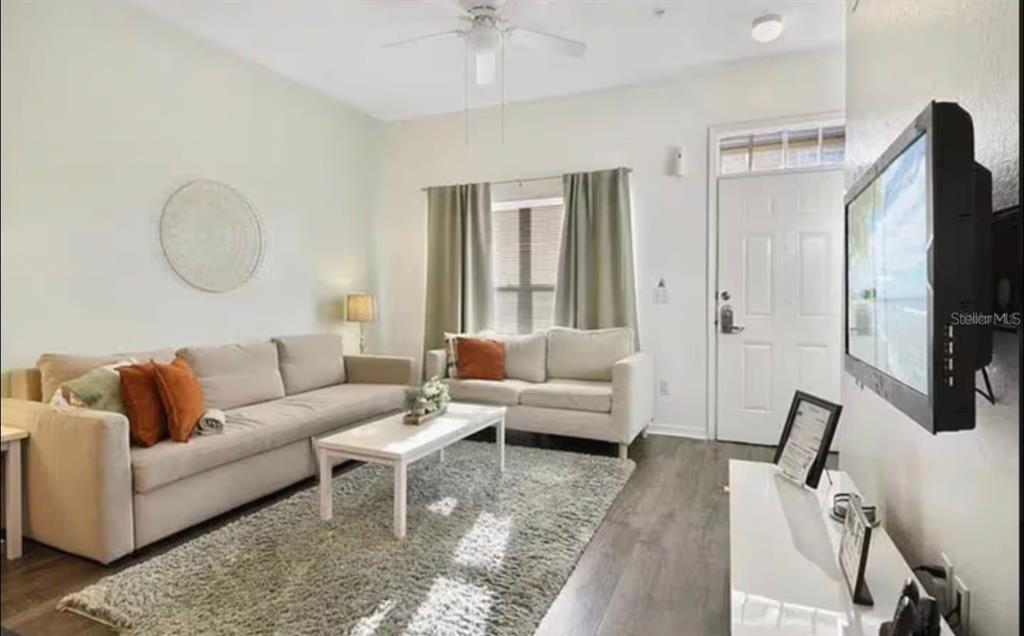 A living room features two beige sofas, a white coffee table, and a wall-mounted television — 4560 E YELLOWGOLD ROAD APT 105, KISSIMMEE, FL