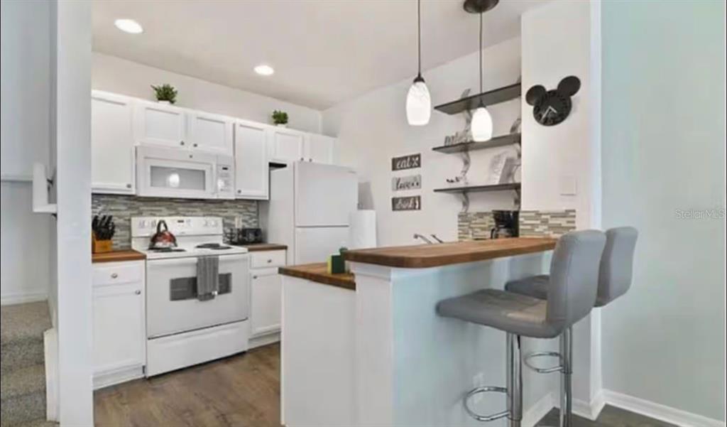 A kitchen features white cabinets, a white stove, a wooden breakfast bar, and two stools — 4560 E YELLOWGOLD ROAD APT 105, KISSIMMEE, FL