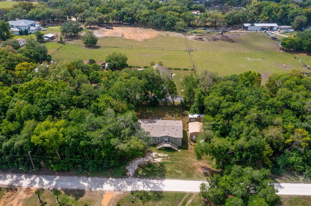 An aerial view shows a house with a deck surrounded by trees and open fields — 38616 COLEEN AVENUE, ZEPHYRHILLS, FL