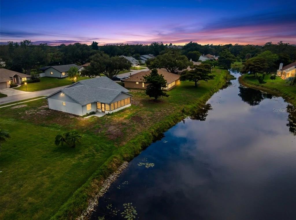 An aerial view shows a suburban house with a screened porch beside a small lake — 112 WOODINGHAM DRIVE, VENICE, FL