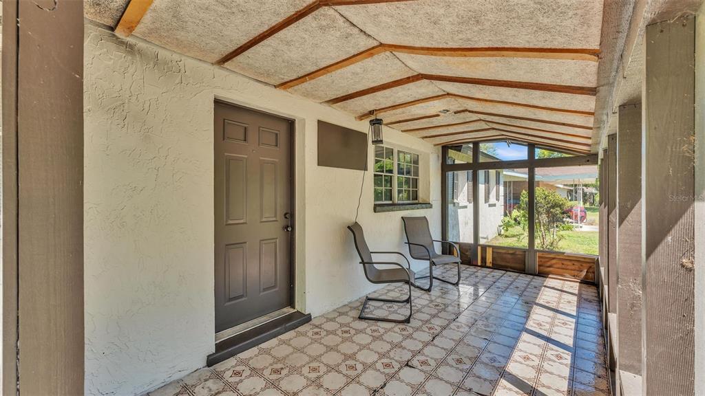 A covered porch with tiled flooring, two chairs, and a brown door — 503 MARIANNA ROAD, AUBURNDALE, FL