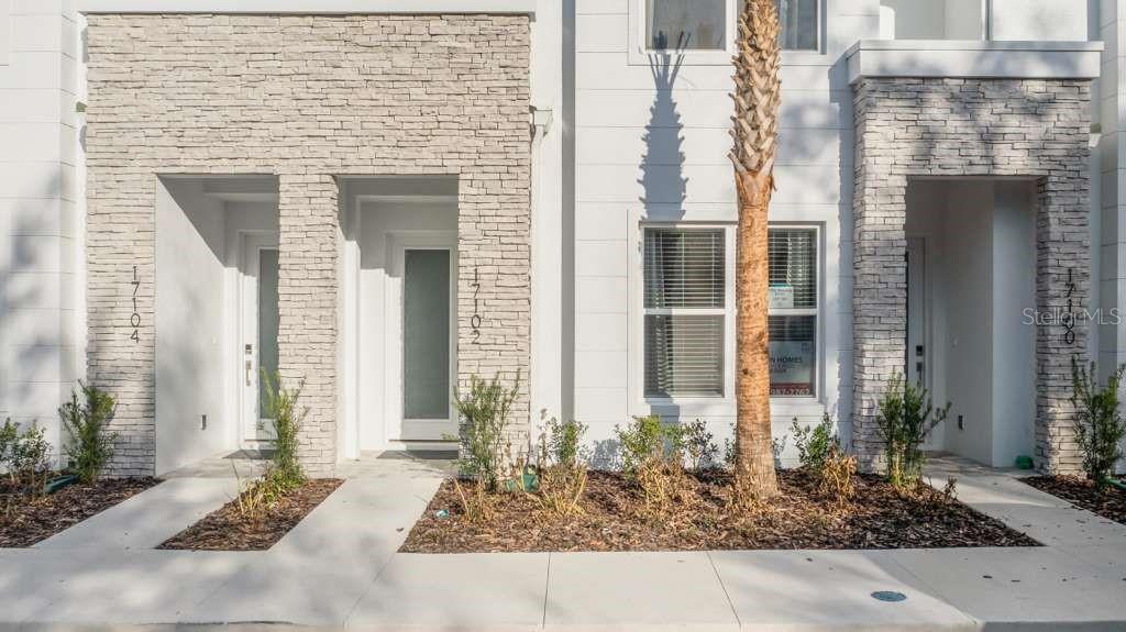 The exterior of a modern townhouse features white siding, stone veneer accents, and small landscaping — 17102 BLESSING DRIVE, CLERMONT, FL