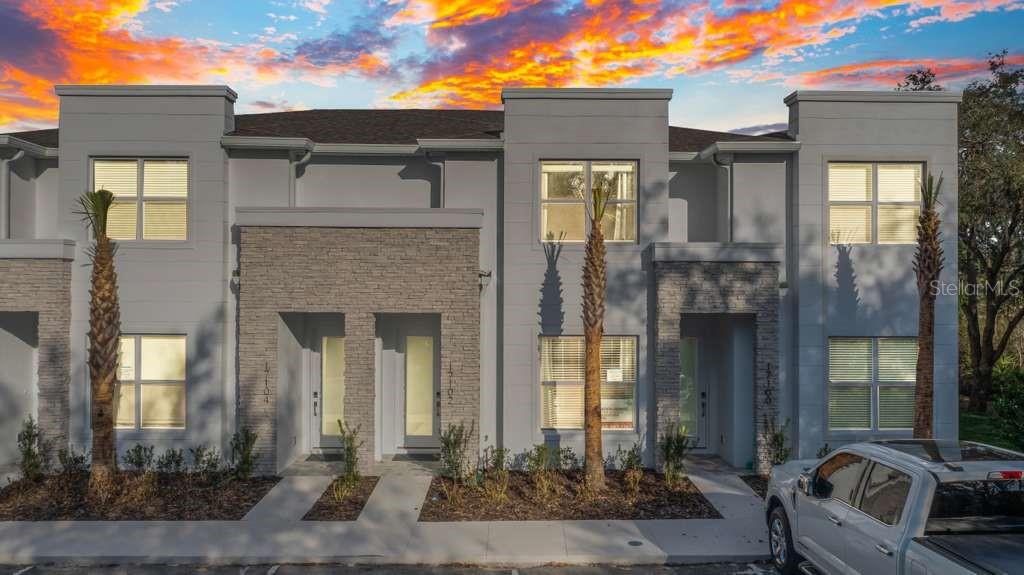 A modern multi-unit townhouse exterior features gray stucco walls, stone accents, and palm trees — 17102 BLESSING DRIVE, CLERMONT, FL