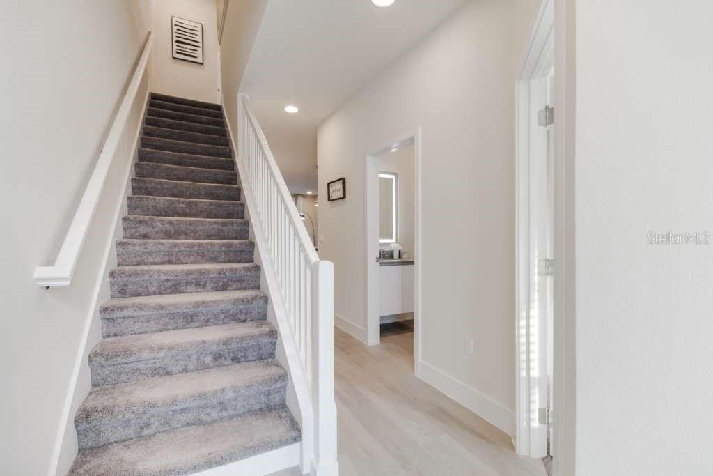 A carpeted staircase with white railings leads to an upper floor in a bright hallway — 17102 BLESSING DRIVE, CLERMONT, FL