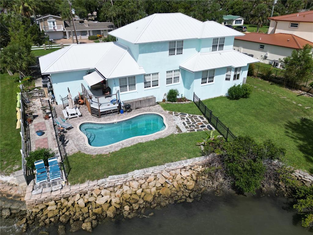 An aerial view of a two-story light blue house with a pool and waterfront bulkhead — 1205 S RIVERSIDE DRIVE, EDGEWATER, FL