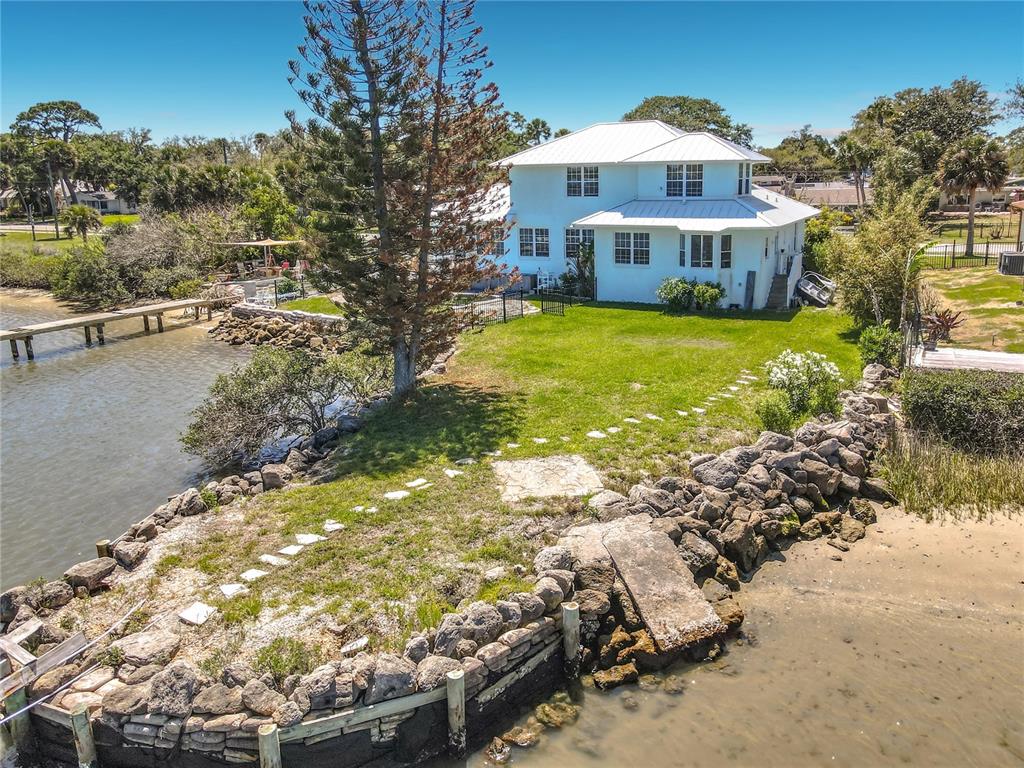A white two-story house sits on a grassy waterfront lot with a stone seawall — 1205 S RIVERSIDE DRIVE, EDGEWATER, FL