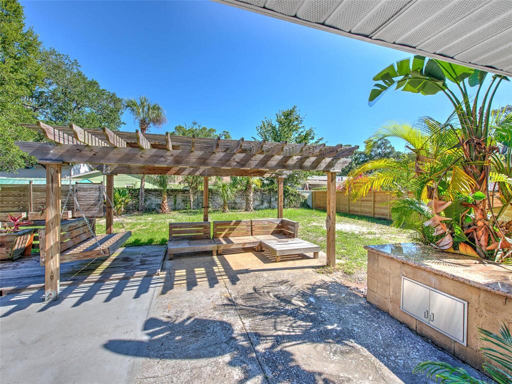 A backyard patio features a wooden pergola, a hanging swing, built-in seating, and a stone counter — 4711 W SAN RAFAEL STREET, TAMPA, FL