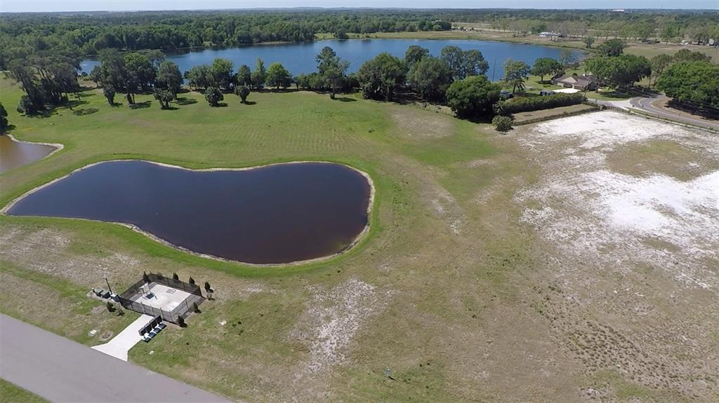 An aerial view shows a grassy lot with a pond, a fenced utility area, and trees — 3412 LAKE DIANE RD #67, TAVARES, FL