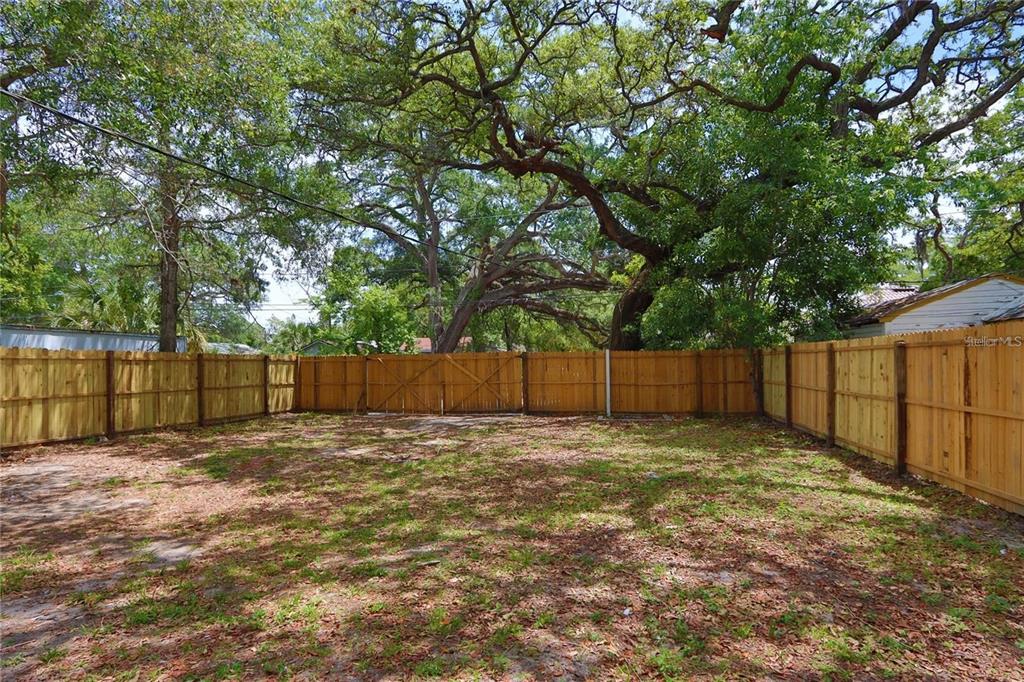 A fenced backyard features a patch of grass and dirt under large, mature oak trees — 1532 13TH STREET S, ST PETERSBURG, FL