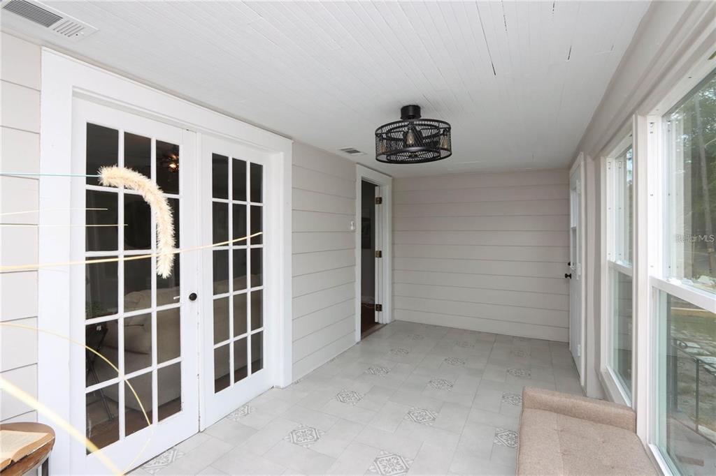 A sunroom with light-colored tile flooring, horizontal wall paneling, and a black cage ceiling light — 1532 13TH STREET S, ST PETERSBURG, FL