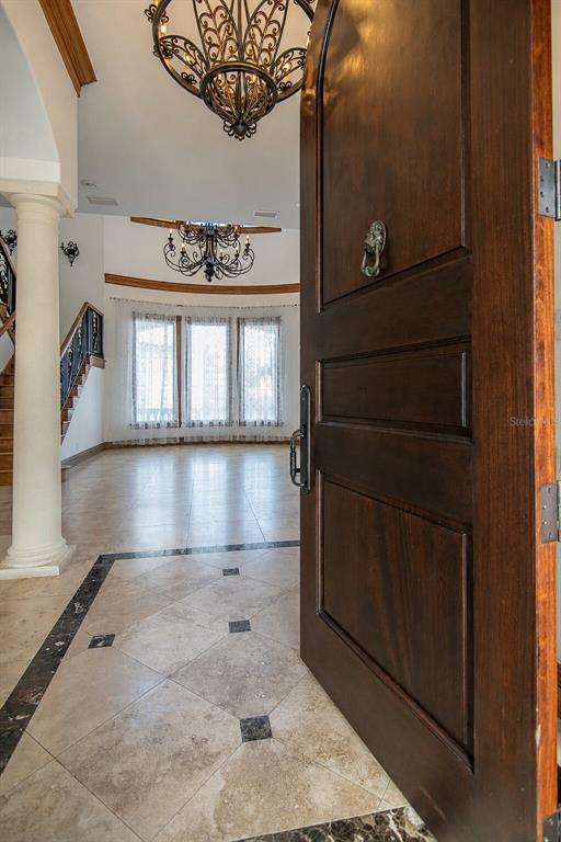 A view through an open wooden door into a tiled foyer with a grand chandelier — 5211 W NEPTUNE WAY, TAMPA, FL