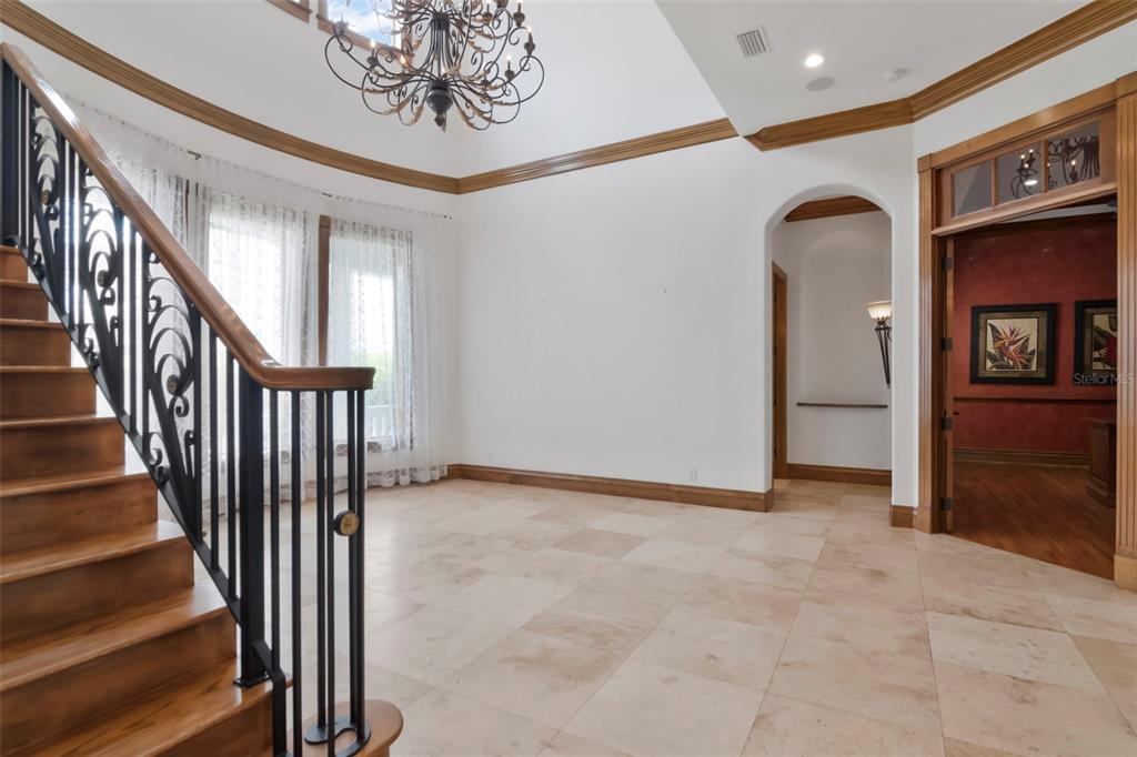 An entryway features a wooden staircase with iron railings, tile flooring, and a chandelier — 5211 W NEPTUNE WAY, TAMPA, FL