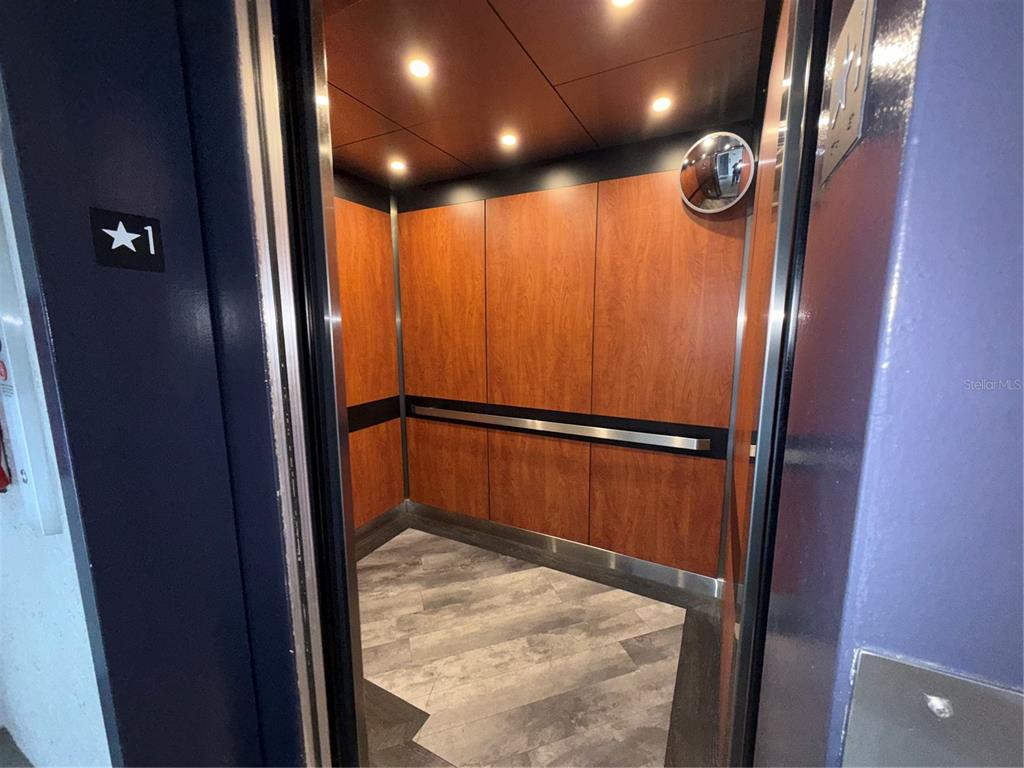 An elevator interior features wood-paneled walls, a metal handrail, recessed lighting, and a convex mirror — 15 ESCONDIDO COURT UNIT 148, ALTAMONTE SPRINGS, FL