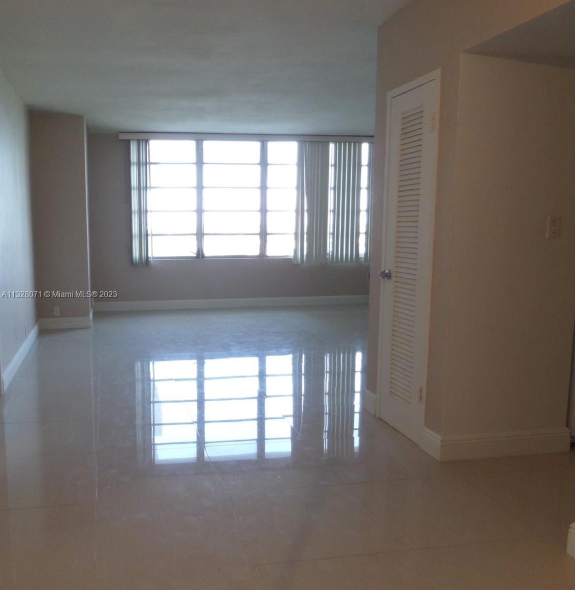 An empty room features light-colored tile flooring, beige walls, and a large window with blinds — 1000 West Ave # 1032, Miami Beach FL 33139, MIAMI BEACH, FL
