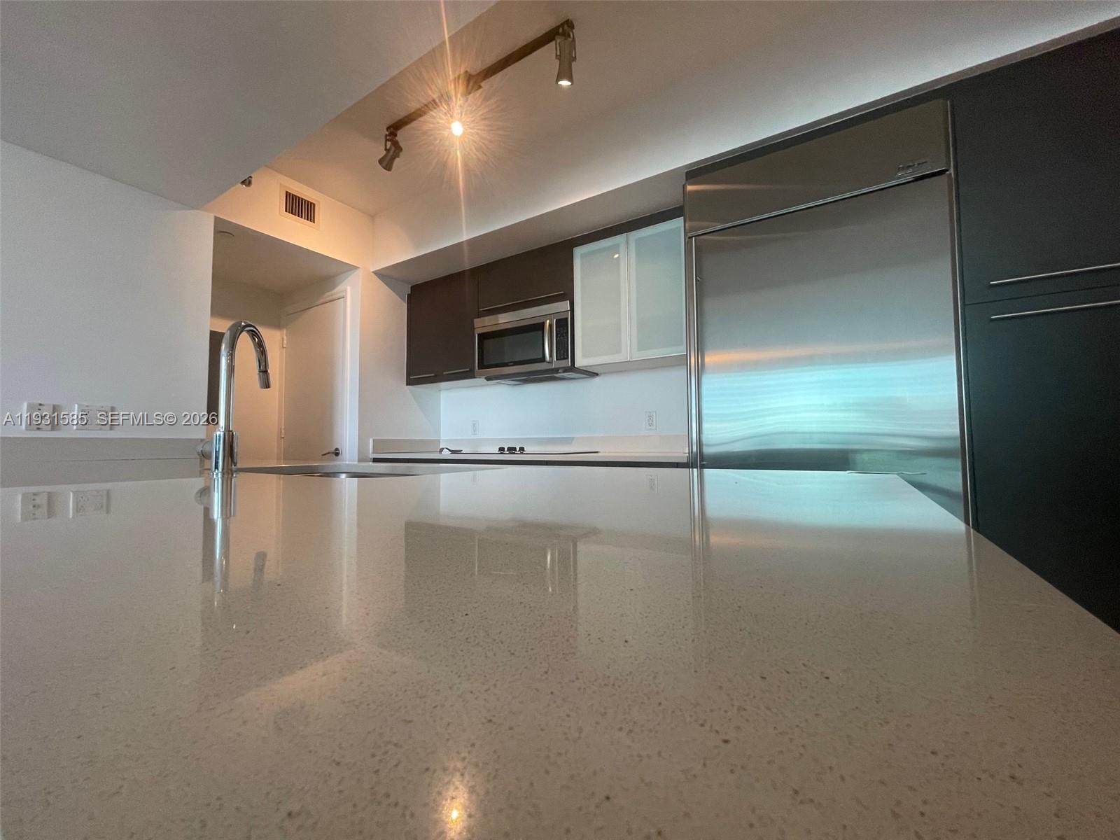 A modern kitchen features a large quartz island, stainless steel refrigerator, and dark cabinetry — 500 Brickell Ave # 3105, Miami FL 33131, MIAMI, FL