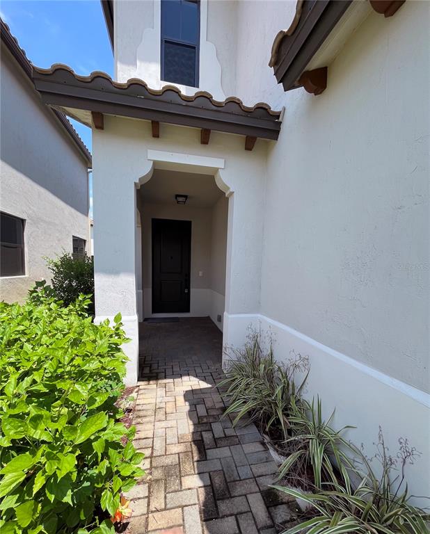 A paved walkway leads to a covered entryway with a dark front door — 5525 AGOSTINO WAY, AVE MARIA, FL