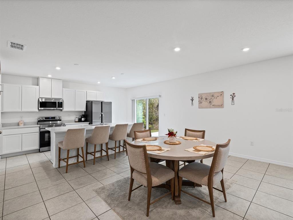 A kitchen with white cabinets and an island flows into a dining area with tile floors — 16334 FROST BIRD ROAD, WEEKI WACHEE, FL