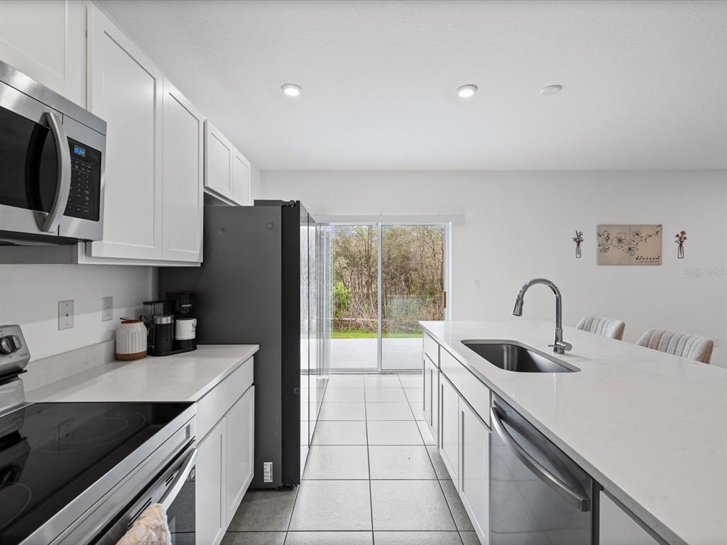 A modern kitchen features white cabinets, stainless steel appliances, a large island, and tile flooring — 16334 FROST BIRD ROAD, WEEKI WACHEE, FL