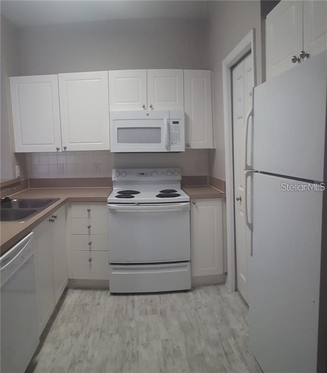 A kitchen features white cabinets, white appliances, a tan countertop, and light-colored wood-look flooring — 5152 NORTHRIDGE ROAD UNIT 204, SARASOTA, FL
