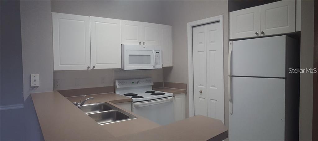 A kitchen features white cabinets, white appliances, and a double-basin sink with tan countertops — 5152 NORTHRIDGE ROAD UNIT 204, SARASOTA, FL