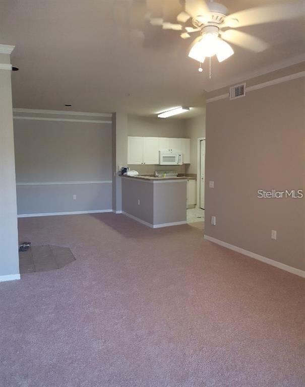A living room with beige carpet leads to an open kitchen with white cabinets — 5152 NORTHRIDGE ROAD UNIT 204, SARASOTA, FL