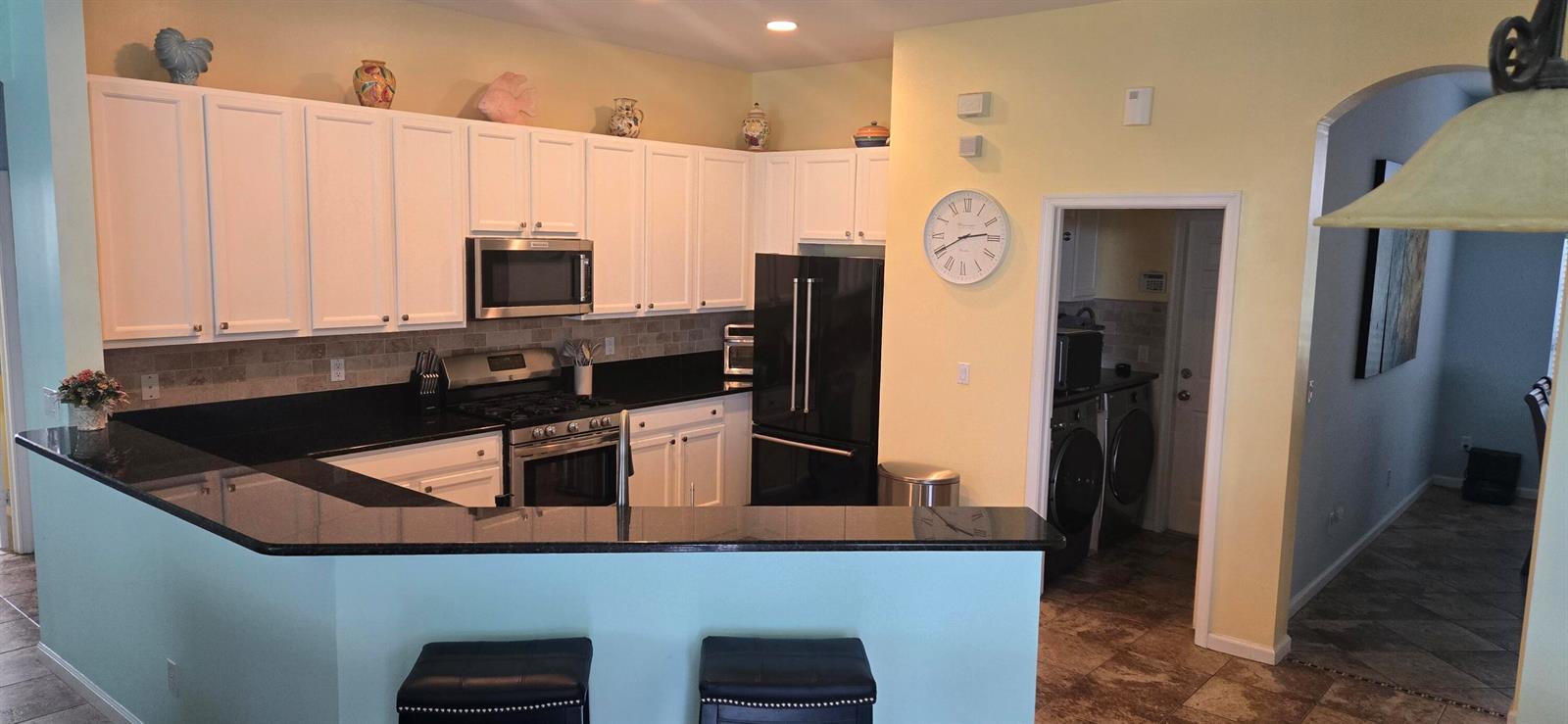 A kitchen features white cabinets, black countertops, stainless steel appliances, and a breakfast bar — 607 Tangelo Circle SW, Vero Beach FL 32968, VERO BEACH, FL