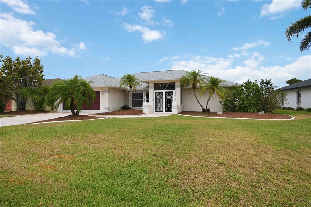 A single-story house with a light-colored exterior, palm trees, and a large front lawn — 63 CLUBHOUSE ROAD, ROTONDA WEST, FL
