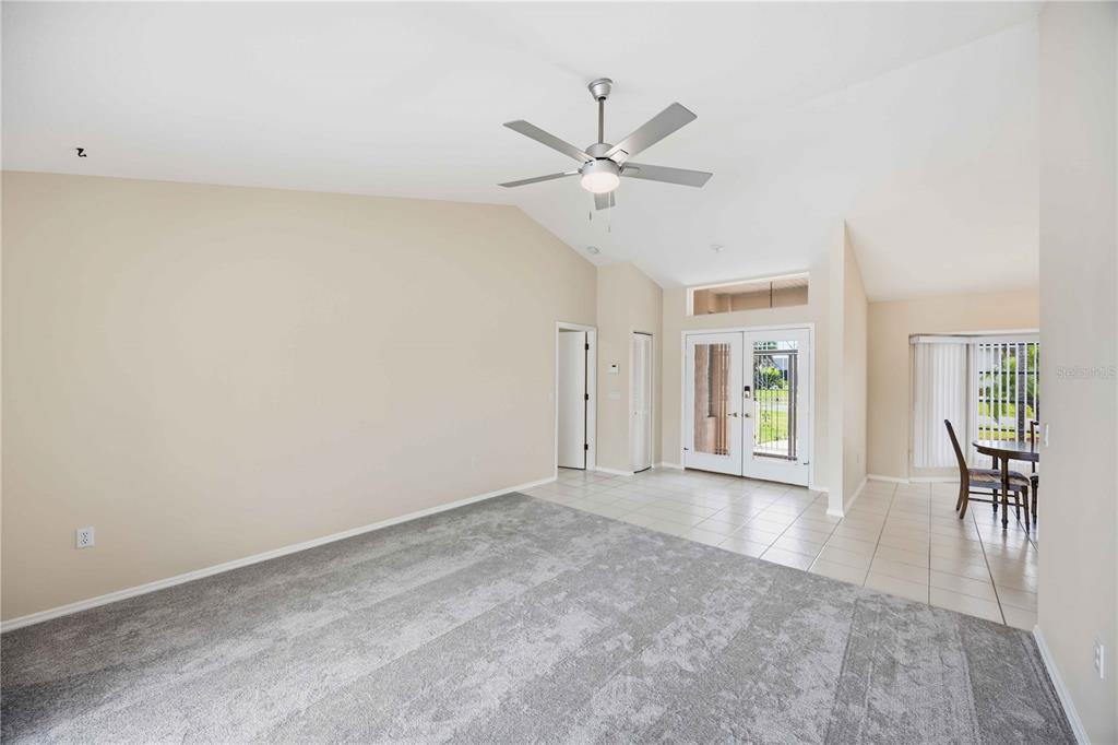 A living room with gray carpeting, a vaulted ceiling, a ceiling fan, and tiled entryway — 63 CLUBHOUSE ROAD, ROTONDA WEST, FL