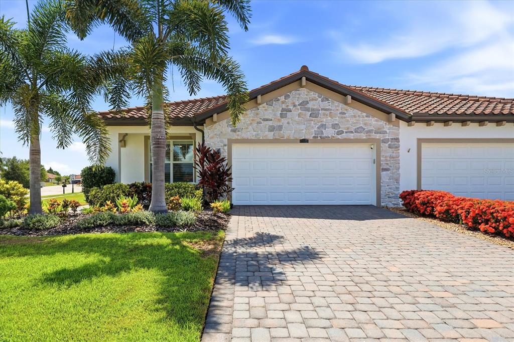 A single-story house exterior featuring a stone facade, a two-car garage, and a paver driveway — 2405 WILDFLOWER RUN, LAKEWOOD RANCH, FL