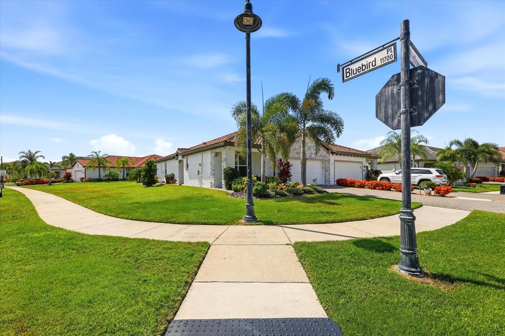 A street corner view shows a single-story house with a lawn and a street sign — 2405 WILDFLOWER RUN, LAKEWOOD RANCH, FL