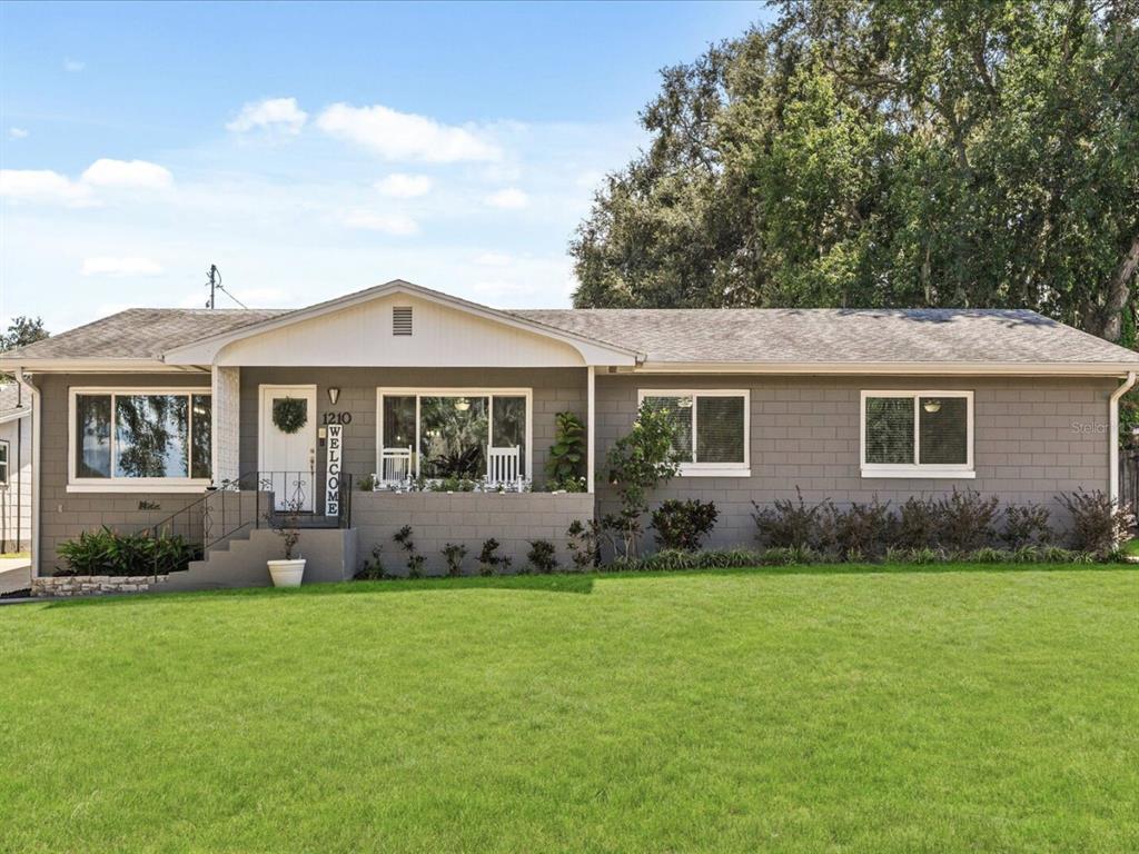 A single-story gray concrete block house features a white front door and a green lawn — 1210 E CAROLINE STREET, TAVARES, FL